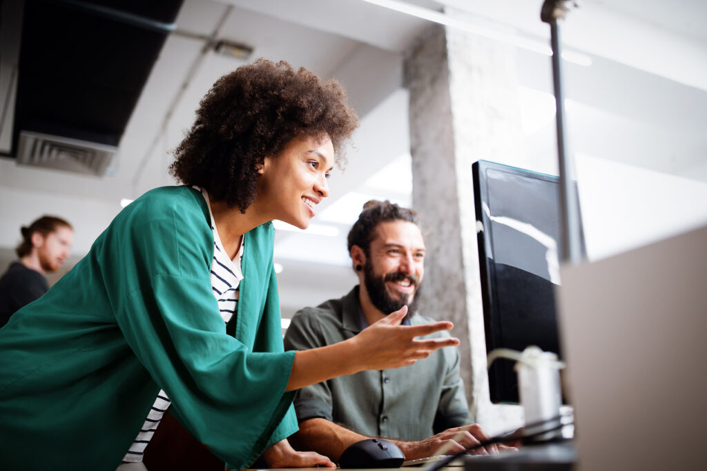 Woman in a teal shirt helping a man sitting at a computer.